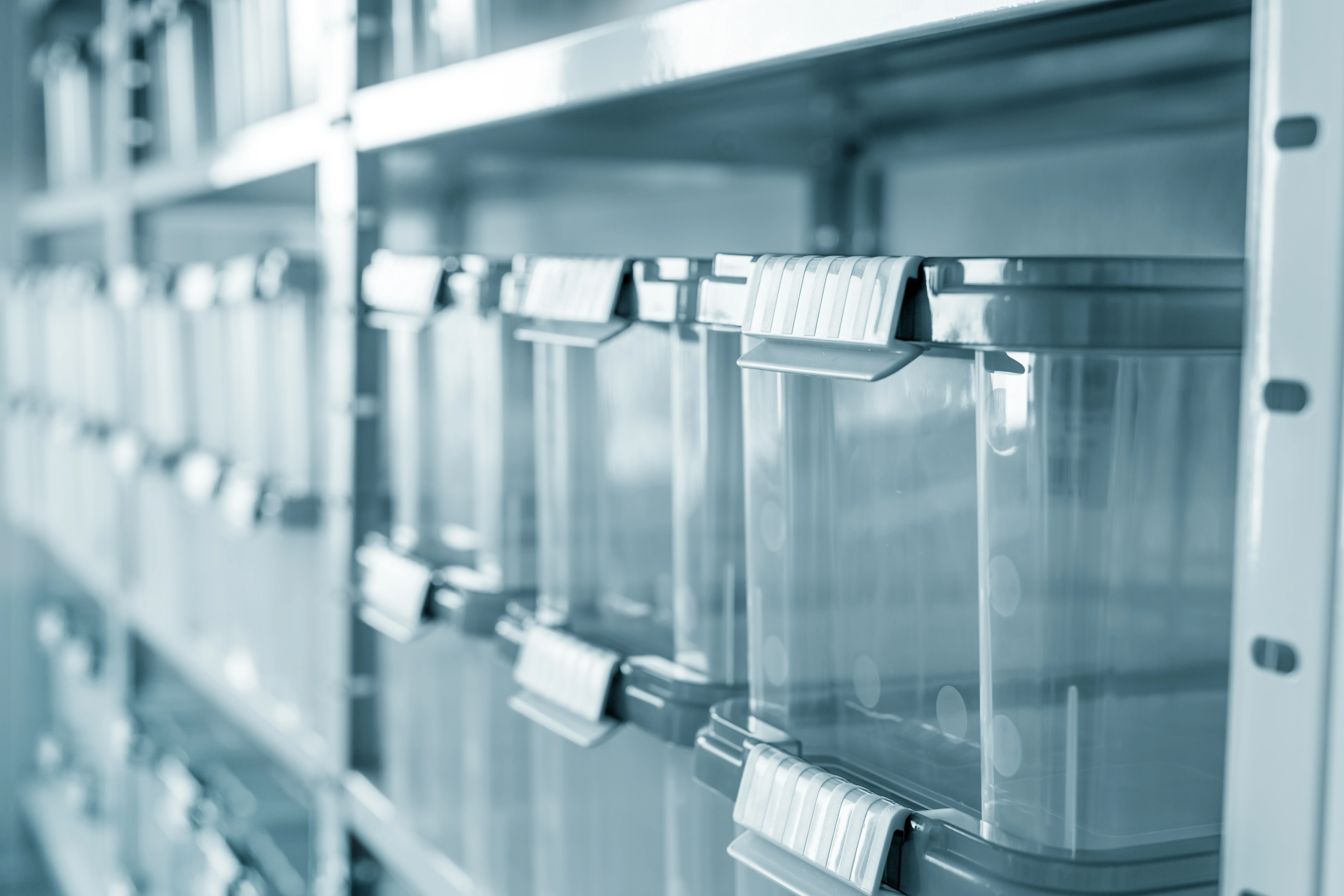 Clear storage containers lined on metal shelves, featuring gray lids with handles, slightly out of focus background for depth.