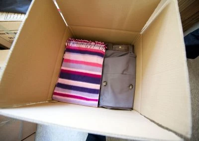 An open cardboard box containing a striped blanket and a pair of gray trousers.