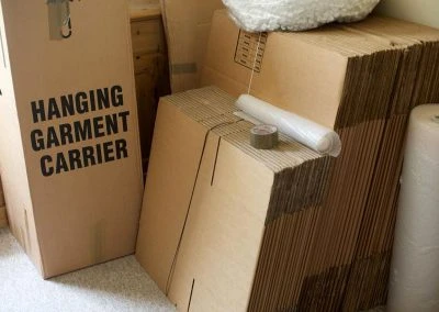 A stack of cardboard boxes, including a hanging garment carrier box and rolls of packing materials, in a storage area.