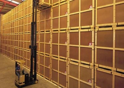 A warehouse interior featuring tall stacks of wooden crates and a forklift positioned in front for lifting and moving items.