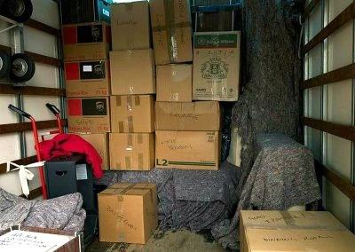 Packed moving truck with stacked boxes, a dolly, and covered furniture, all organized for transport.