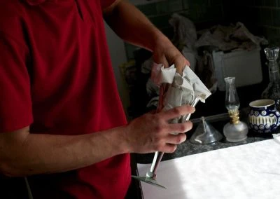 A person in a red shirt carefully unwraps a delicate object in a kitchen setting, surrounded by various glassware and utensils.