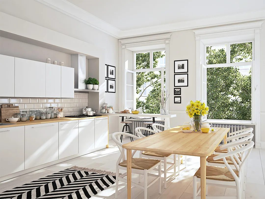 Bright modern kitchen with white cabinetry, wooden countertops, a dining table with yellow flowers, and large windows revealing greenery outside.2