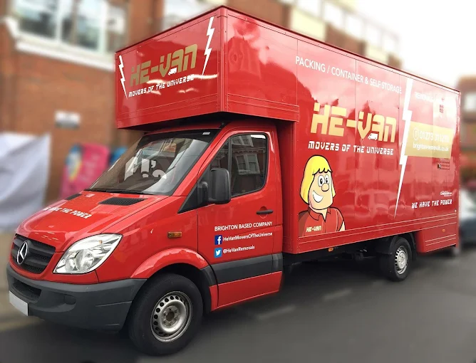 Bright red moving truck with "HE-VAN: Movers of the Universe" branding and cartoon character illustration, parked in an urban area.